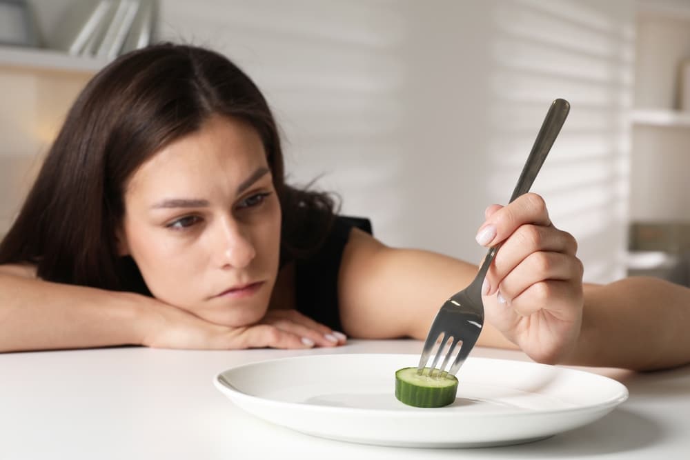 Eating,Disorder.,Sad,Woman,Holding,Fork,With,Cucumber,At,Table